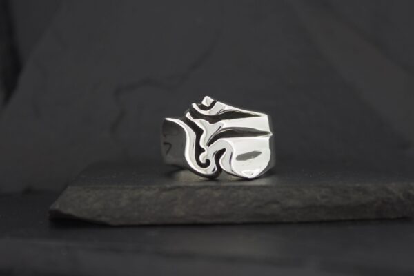 A silver ring with an abstract, artistic design on a dark background.