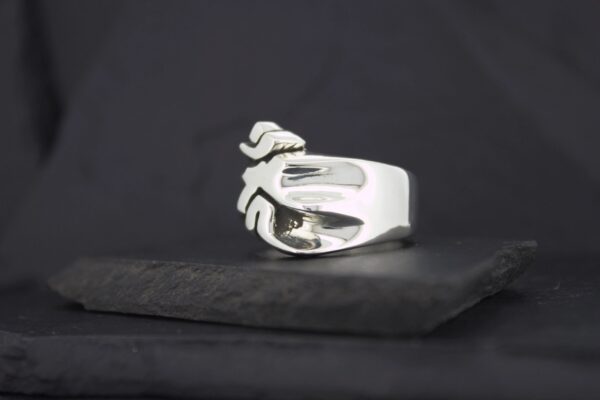 A silver ring shaped like a hand on a dark background.