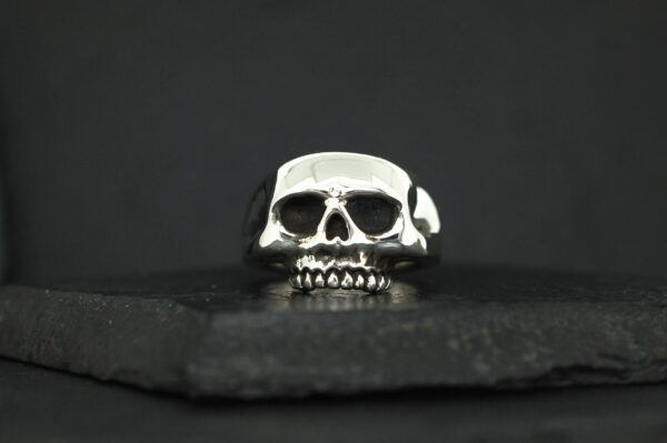 A silver skull-shaped ring against a dark background.