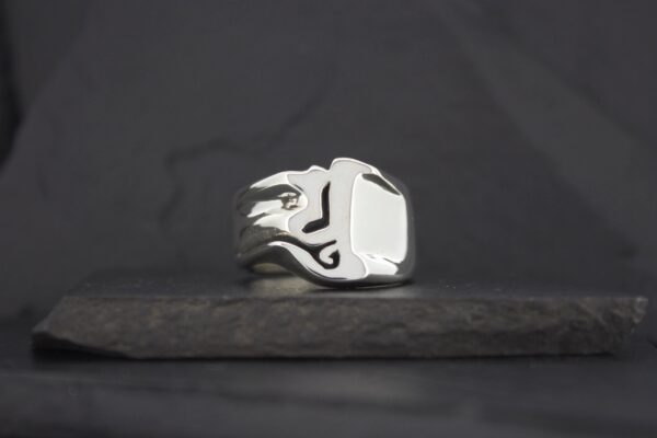 A silver ring with a flame design on a dark surface.