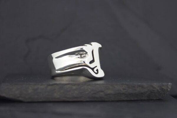 A silver ring with a unique, abstract design on a dark surface.