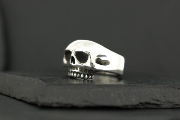 A silver skull ring on a dark surface.