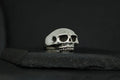 A silver ring shaped like a skull on a dark surface.