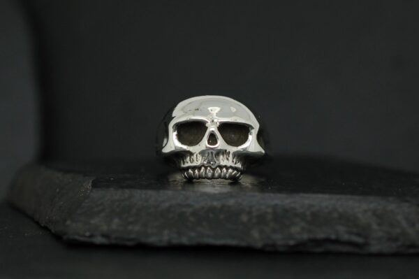 A small, metallic skull placed on a dark surface with a black background.