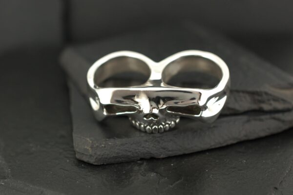 Silver double-finger ring with a heart detail on black fabric.