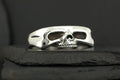Silver ring with a skull design on a dark surface.