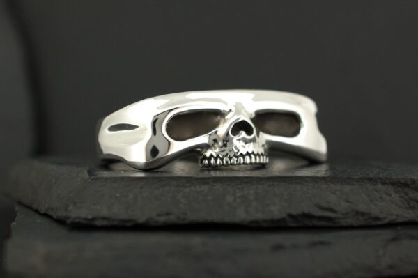 Silver ring with a skull design on a dark surface.