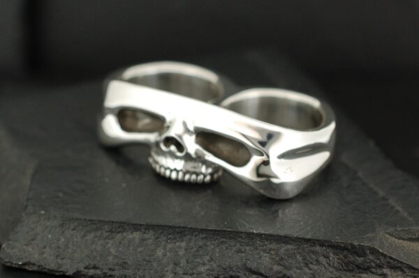 Silver skull-shaped double-finger ring with intricate details.