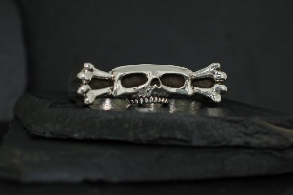 Silver skull and crossbones ring on a dark surface.