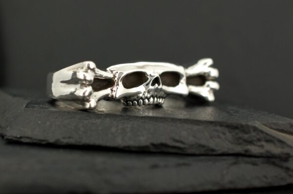 A silver skull ring with crossbones on a black surface.