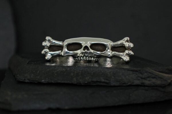 Silver skull and crossbones ring on dark slate surface.