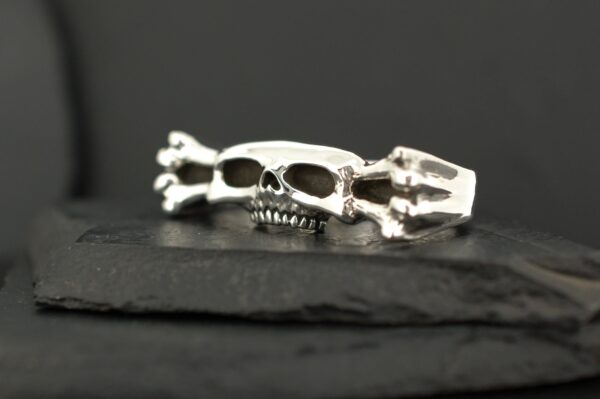 Close-up of a silver skull ring on a dark surface.