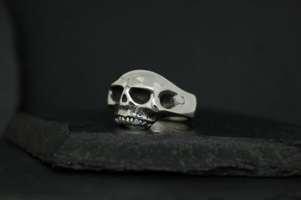 Silver skull ring with sunglasses on a dark background.