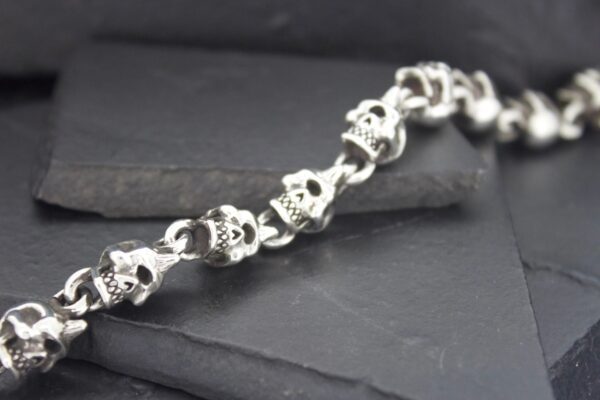 Silver skull chain bracelet on a dark surface.