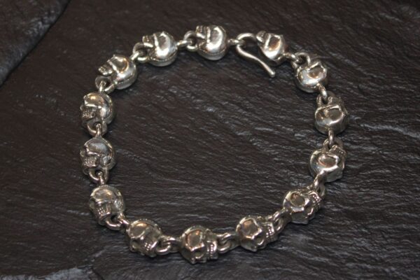 Silver skull bracelet with a lobster clasp on a dark background.