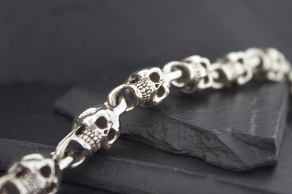 Close-up of a silver skull bracelet on a dark surface.