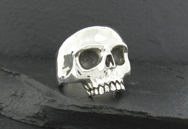 A shiny silver skull ring on a dark surface.