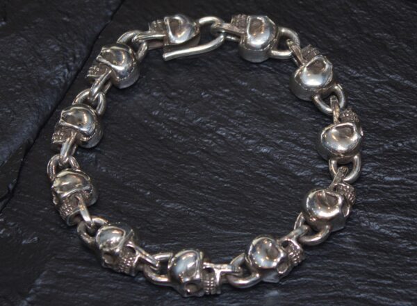 Silver bracelet with skull-shaped links on a dark surface.