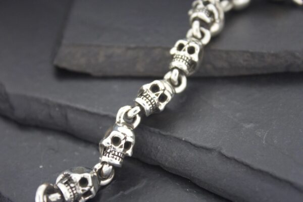 Close-up of a silver skull-themed bracelet on dark stones.
