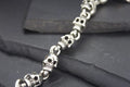 Close-up of a silver skull-themed bracelet on dark stones.