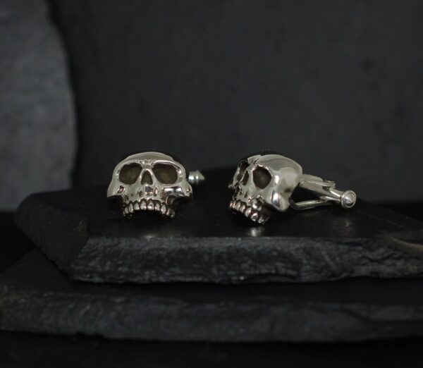 Silver skull cufflinks on a dark surface.