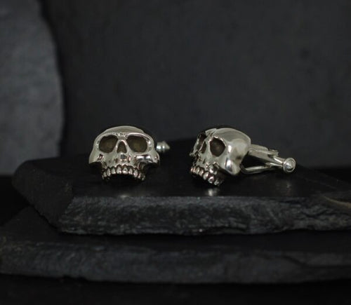 Silver skull cufflinks on a dark surface.