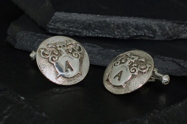 Close-up of silver cufflinks with engraved 'A' initials and ornate designs.