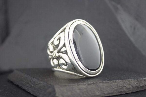 Elegant silver ring with a large black oval stone and intricate floral details.