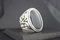 Elegant silver ring with a large black oval stone and intricate floral details.