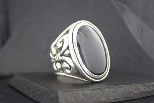 Elegant silver ring with a large black oval stone and intricate floral details.