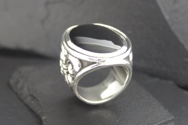A unique silver ring with an open, intertwined design on a dark surface.