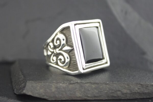 Elegant silver ring with black rectangular stone and intricate side design.