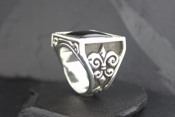 Silver ring with intricate black stone and scrollwork design.