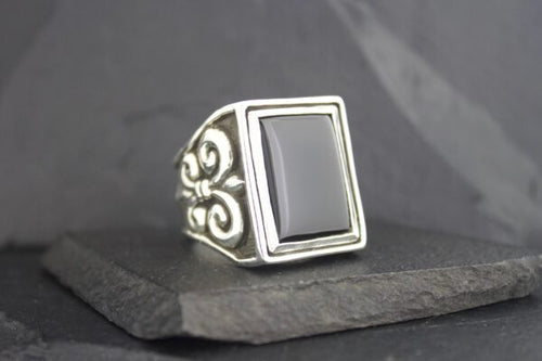 Silver ring with a rectangular black stone and ornate side details.