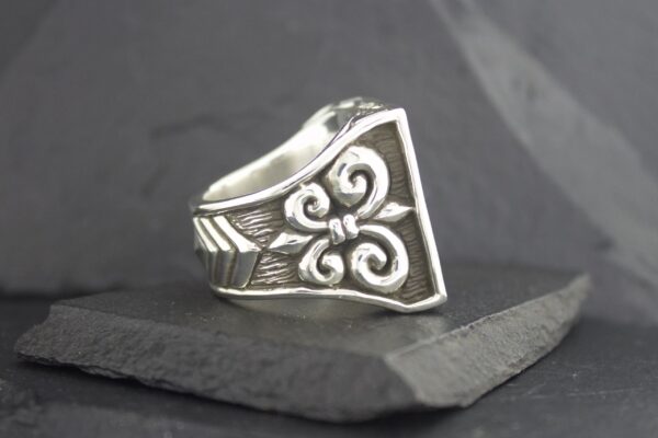 Silver ring with intricate floral design on a slate surface.
