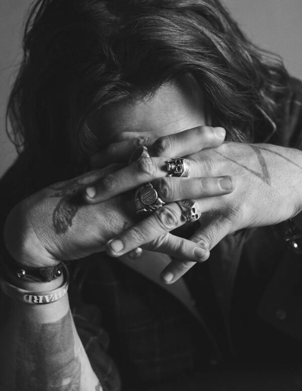 Person hiding face behind hands adorned with rings in black and white.