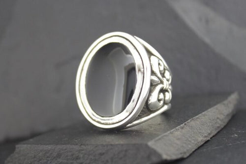 Silver ring with ornate floral design and empty oval bezel.