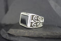 Elegant silver ring with a black square stone and intricate swirl designs.