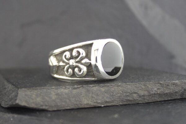 Silver ring with black stone and fleur-de-lis design.
