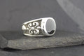 Silver ring with black stone and fleur-de-lis design.