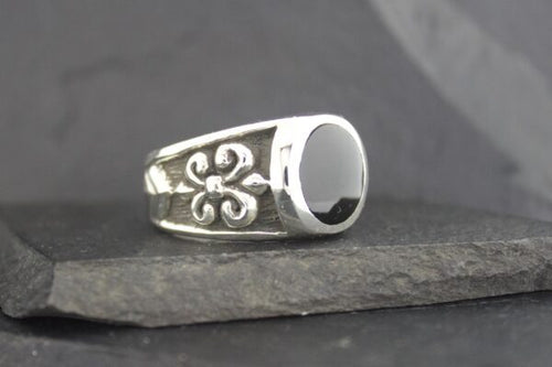 Silver ring with black stone and fleur-de-lis design.