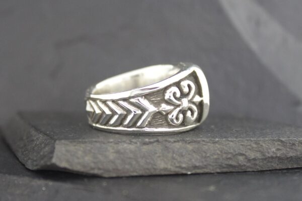 Silver ring with intricate arrow and fleur-de-lis designs.