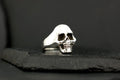 Silver skull ring with detailed features against black background.