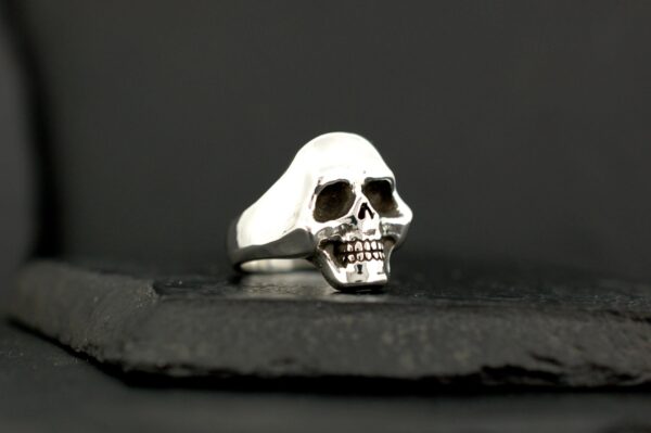 Silver skull ring with detailed features against black background.