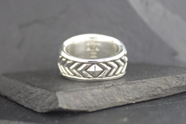 Silver ring with geometric patterns on a dark slate surface.