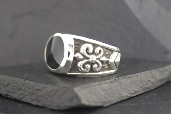 Silver ring with a fleur-de-lis design on a dark surface.