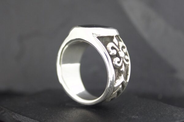 Silver ring with intricate floral design on a dark background.