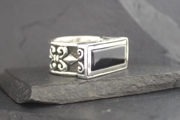 Silver ring with a black rectangular stone and intricate side designs.
