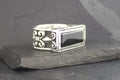 Silver ring with a black rectangular stone and intricate side designs.