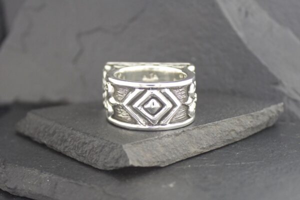 Silver ring with intricate geometric patterns on a dark stone surface.